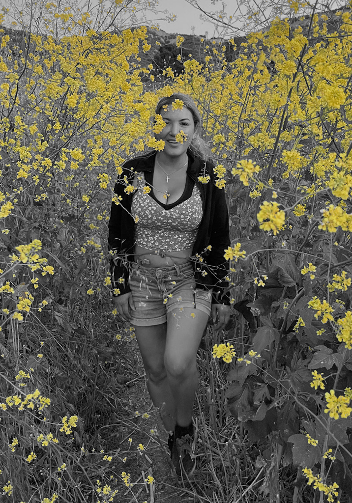 Picture of a woman in black and white walking through yellow flowers.